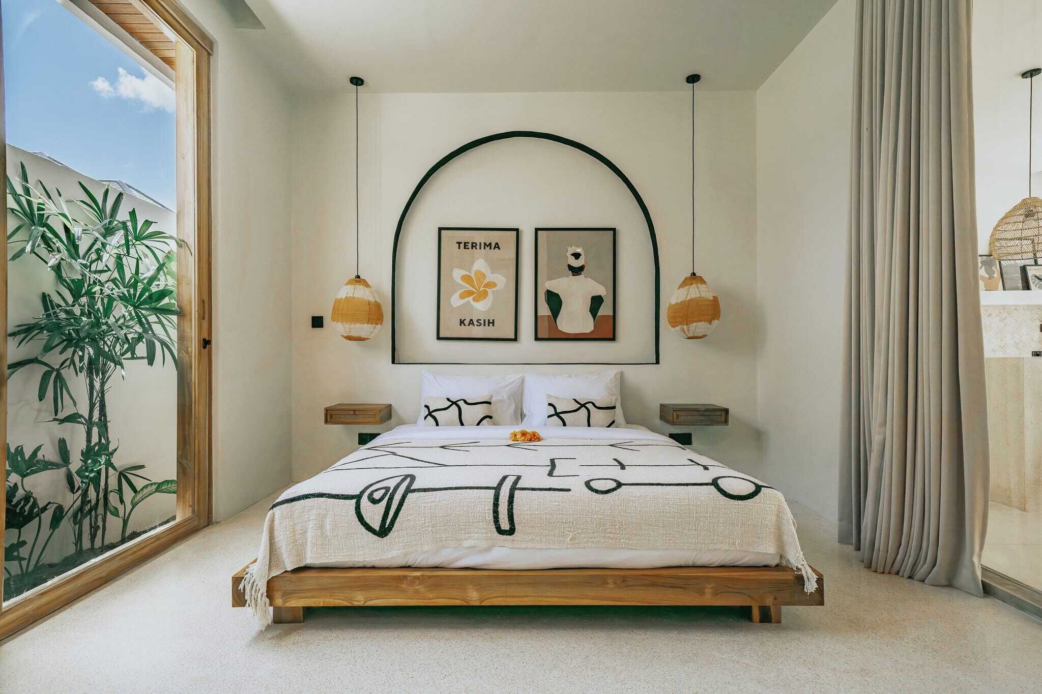 A bedroom with a wooden bed, a large window, a plant, and two wall-mounted lamps.