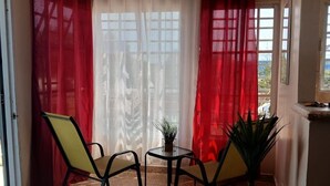 Ein Zimmer mit Fliesenboden, zwei Stühle, einem kleinen Tisch mit Pflanze und roten Vorhängen.