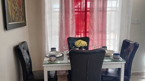 Ein Essbereich mit Tisch für zwei Personen, Stühlen, einer Blumenvase und einem Bild an der Wand.
