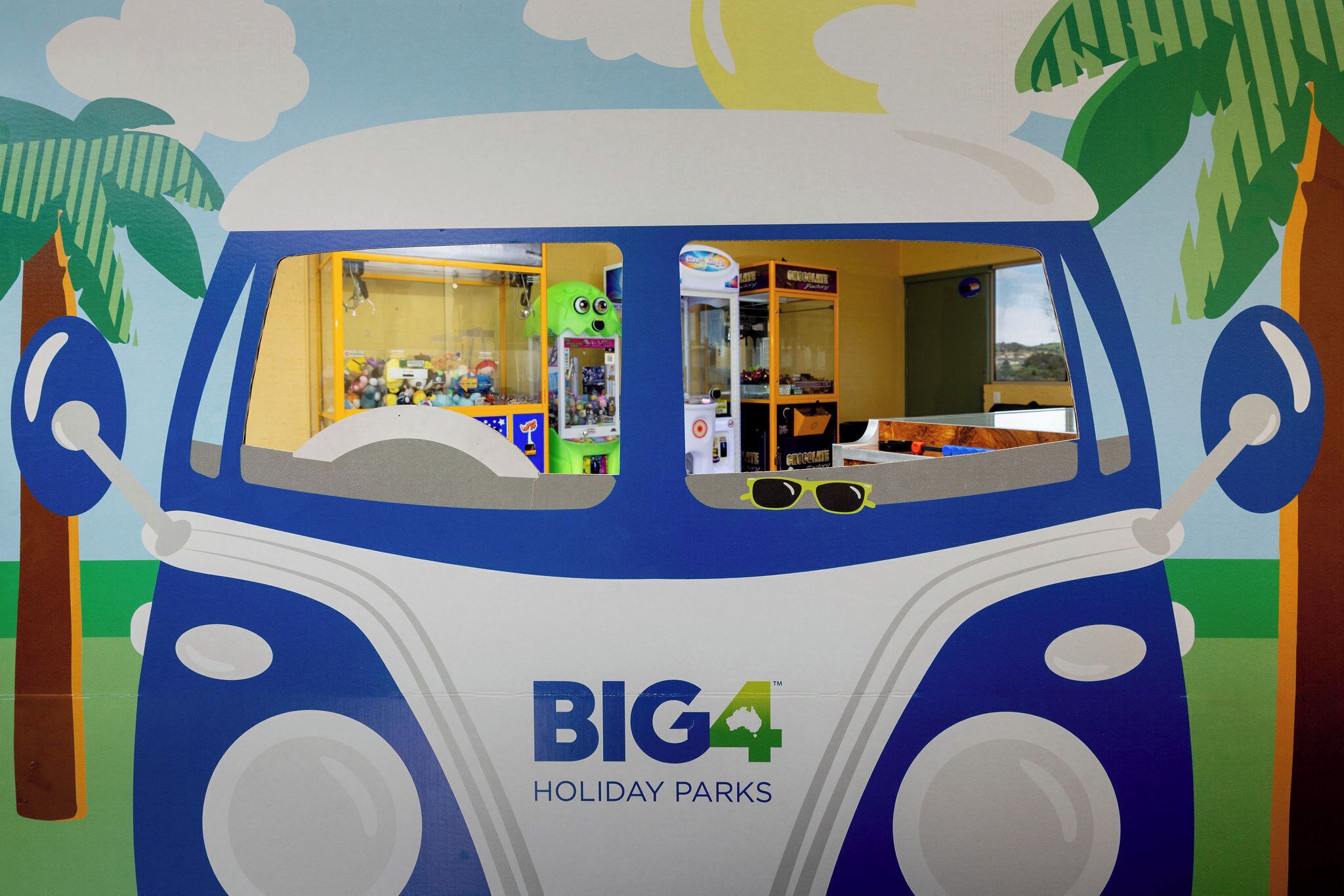 Un véhicule aux couleurs vives, avec l’inscription « BIG4 HOLIDAY PARKS », des jouets exposés dans les vitrines et un palmier sur le côté gauche.