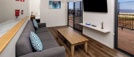 Un salón moderno con sofá, una mesa de madera, televisor y un balcón con vistas.