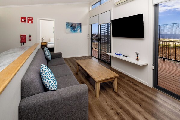 Un salón moderno con sofá, una mesa de madera, televisor y un balcón con vistas.