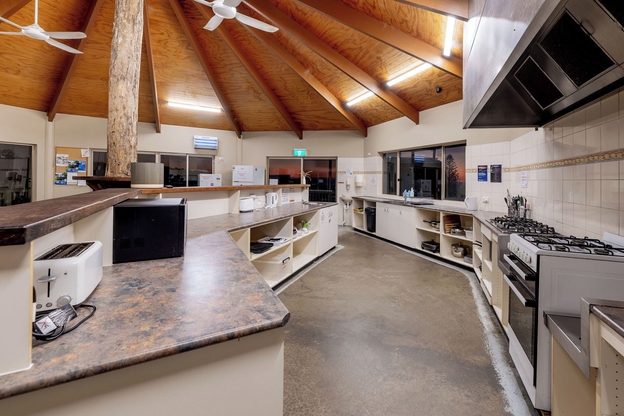 A kitchen with a wooden ceiling, a gas stove, a coffee machine, and a toaster.