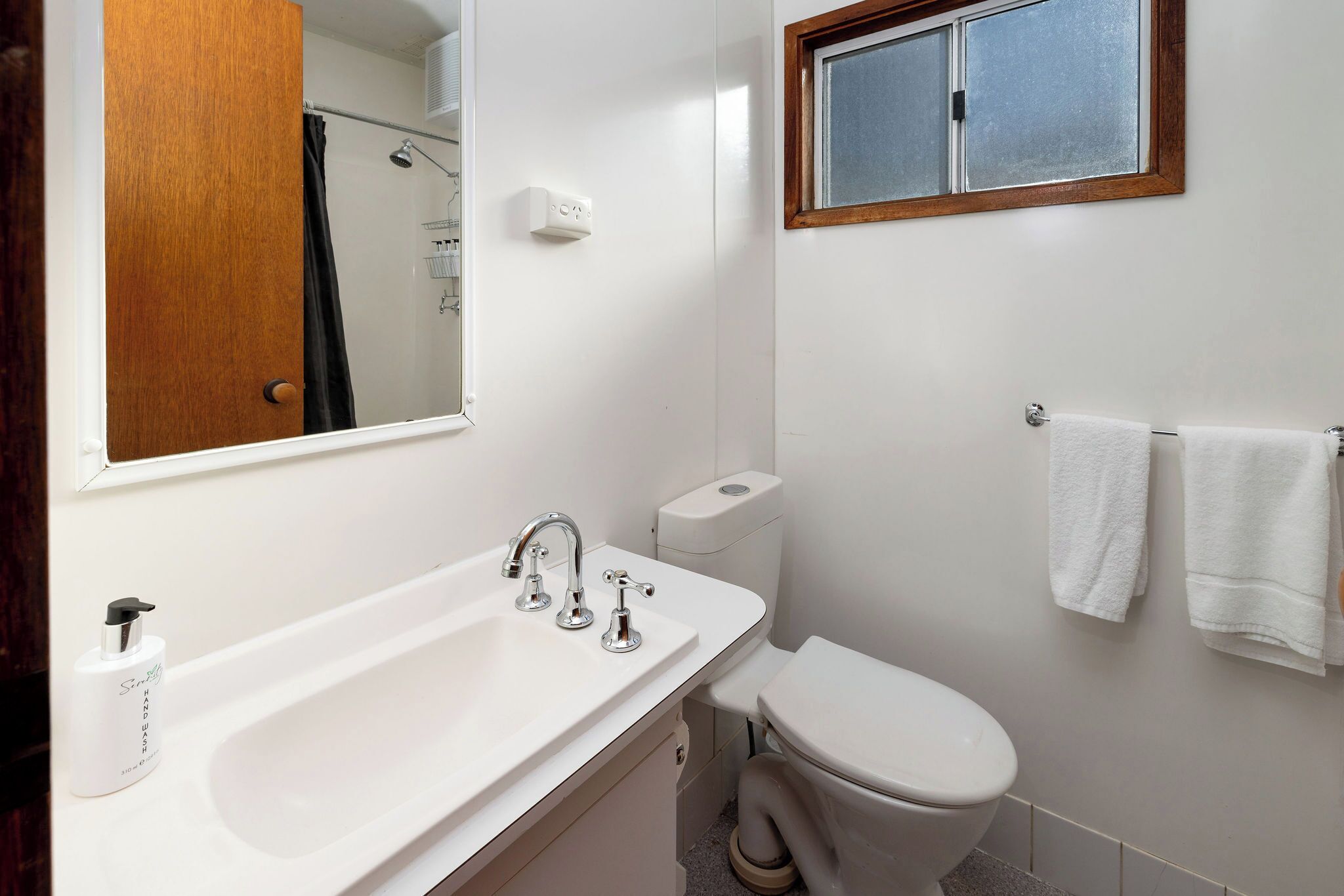 Une salle de bain avec un lavabo blanc, des toilettes, un miroir et une fenêtre.