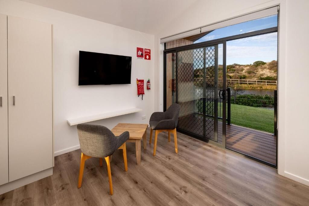 Une chambre moderne dotée d’un téléviseur à écran plat fixé au mur, d’une petite table avec deux chaises et d’une porte-fenêtre coulissante donnant sur un espace extérieur avec vue sur le paysage.