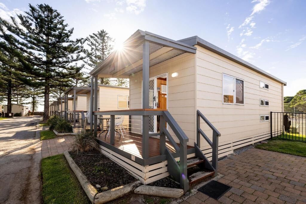 A single-story mobile home with a covered porch, a small outdoor seating area, and a paved driveway.