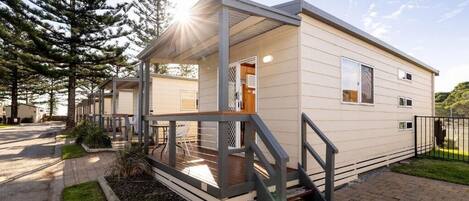 A single-story mobile home with a covered porch, a small outdoor seating area, and a paved driveway.