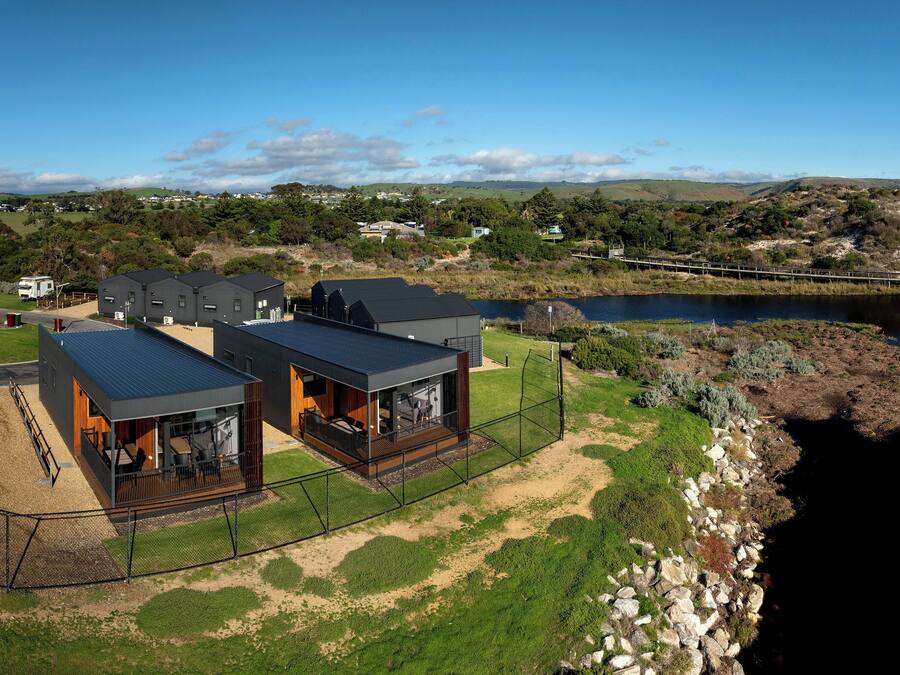 A modern house with a large deck, a fenced yard, and a view of a lake and bridge.