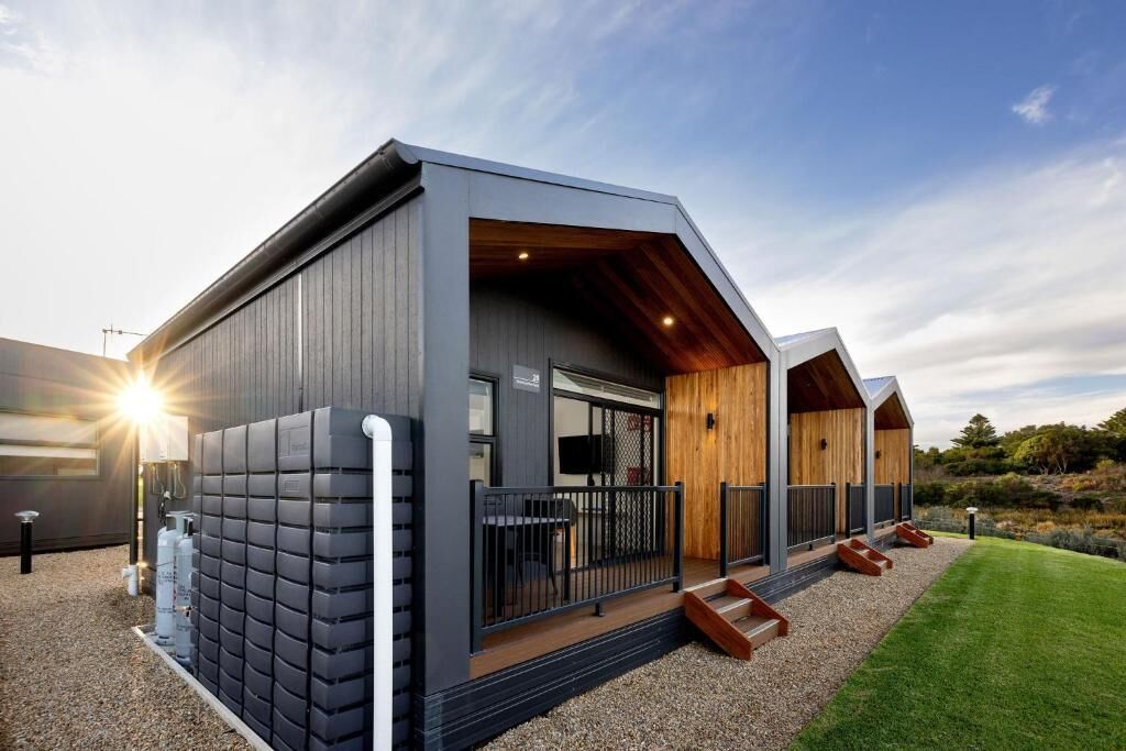 A modern building with a large glass entrance, a wooden deck, and a gravel pathway.