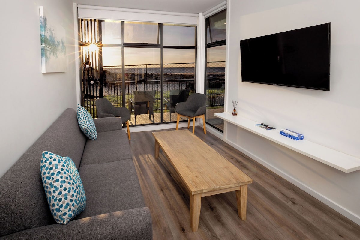 Una sala moderna con sofá, sillas, una mesa de centro, televisor y un balcón con vistas.