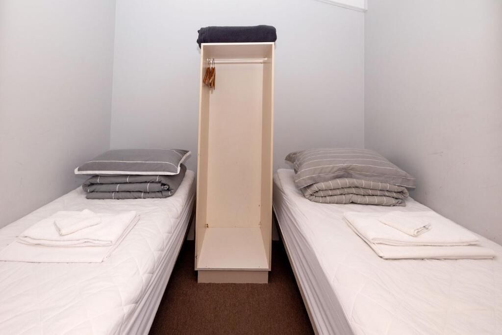 A small, narrow room with two single beds, each with a pillow and a folded blanket.