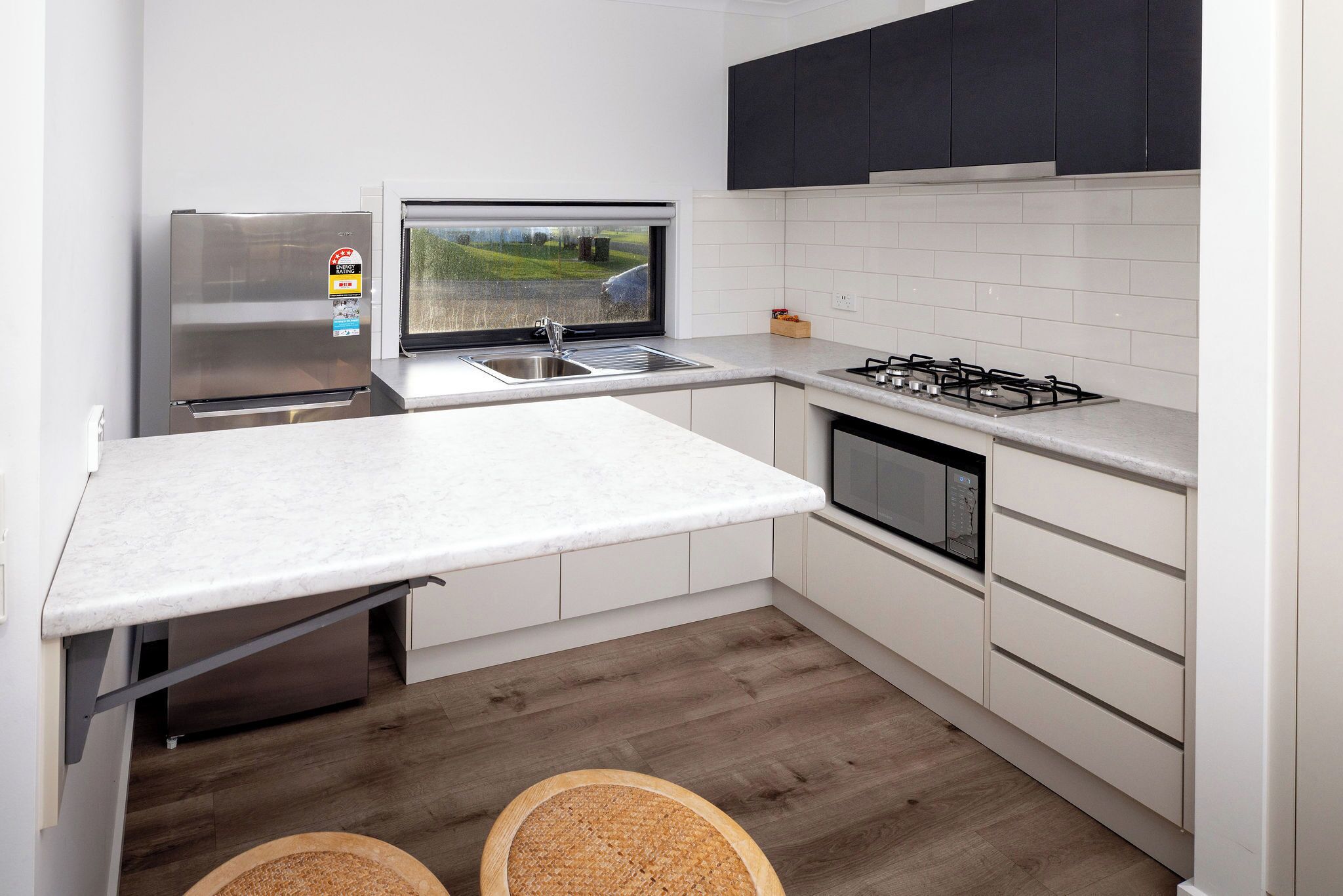 A modern kitchen with a built-in oven, a stainless steel refrigerator, a window with a view, and a gas stove.