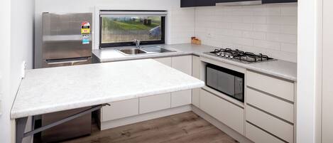 A modern kitchen with a built-in oven, a stainless steel refrigerator, a window with a view, and a gas stove.