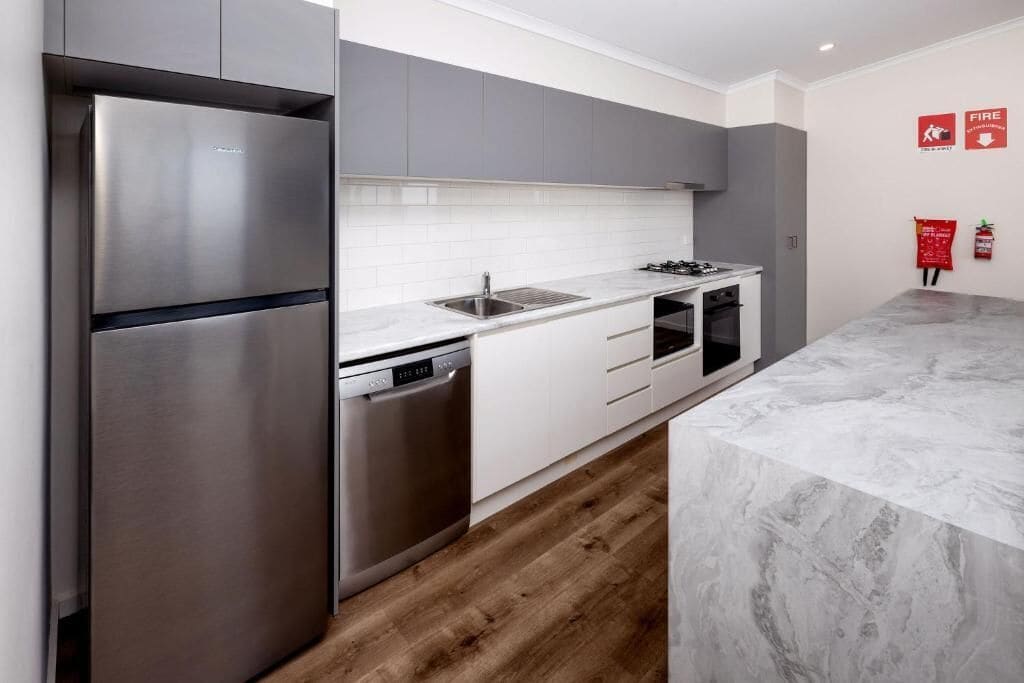 A modern kitchen with stainless steel appliances, white cabinetry, and a marble countertop.