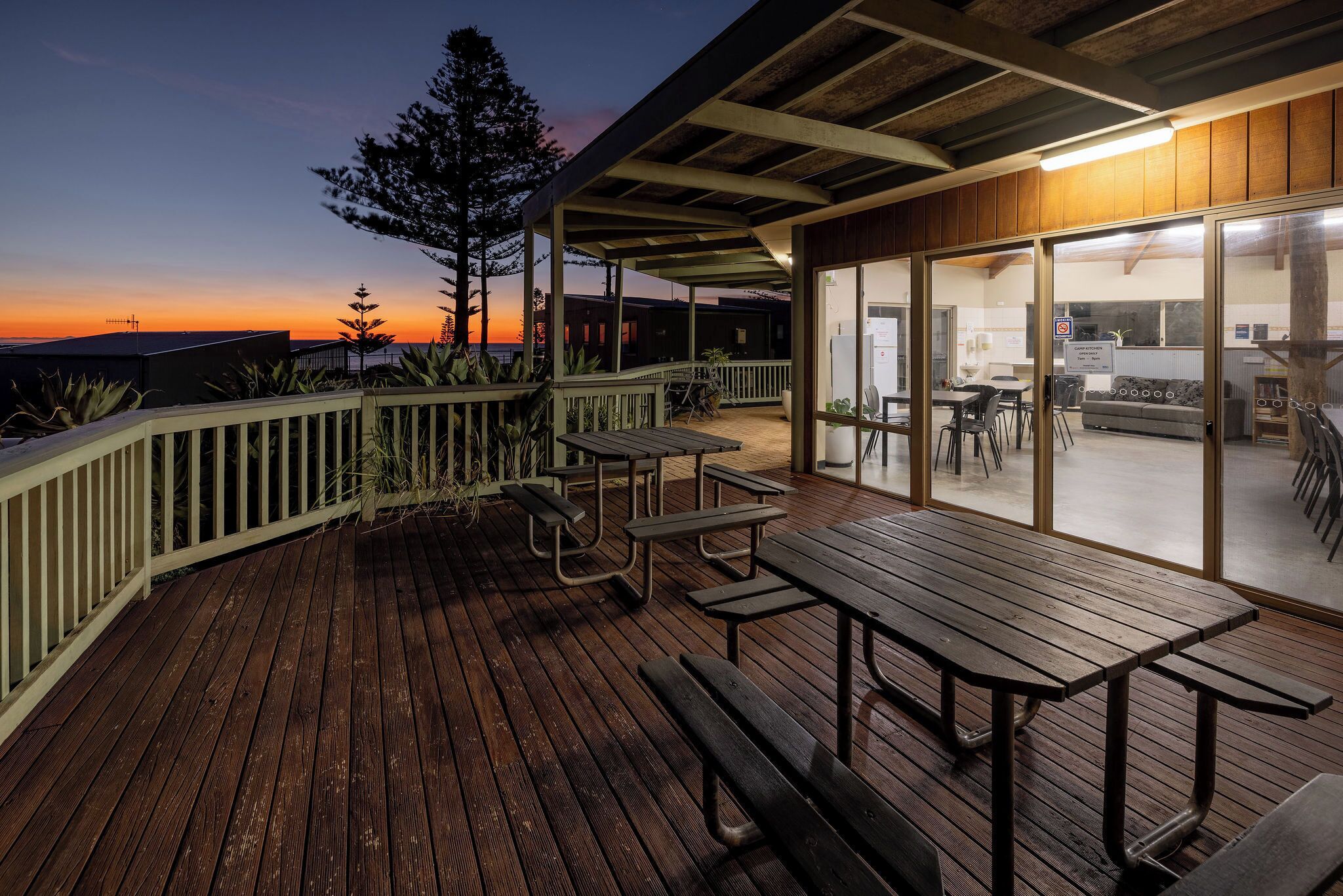 A wooden deck with picnic tables and a covered area with glass doors.
