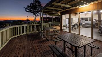 A wooden deck with picnic tables and a covered area with glass doors.