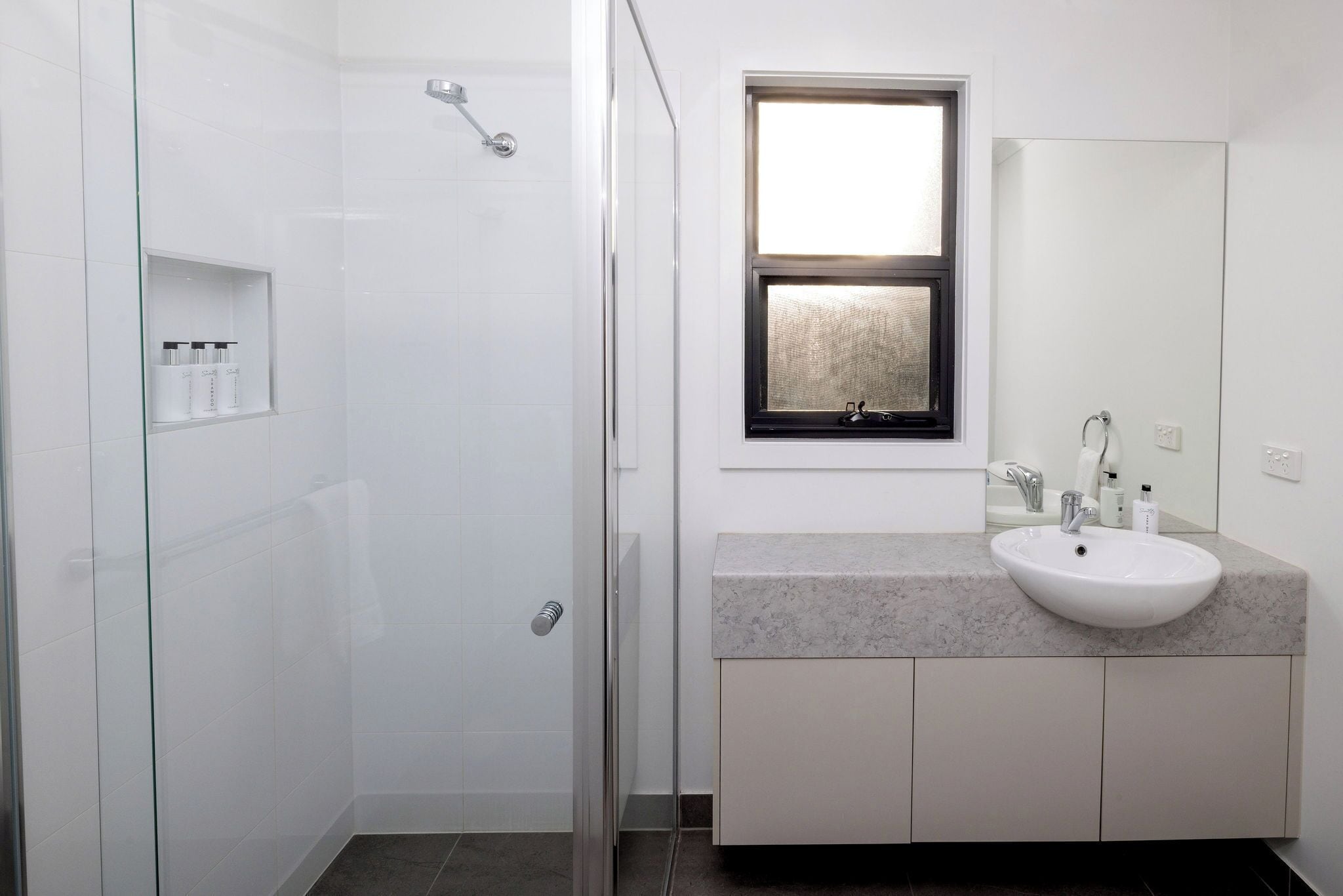 A bathroom with a glass-enclosed shower, a sink with a mirror above, and a window with a view.