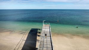 Un muelle que se adentra en un mar azul y despejado, con una playa de arena.
