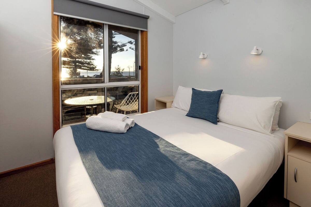 A hotel room with a bed, a window with a view, a small table, and a chair.