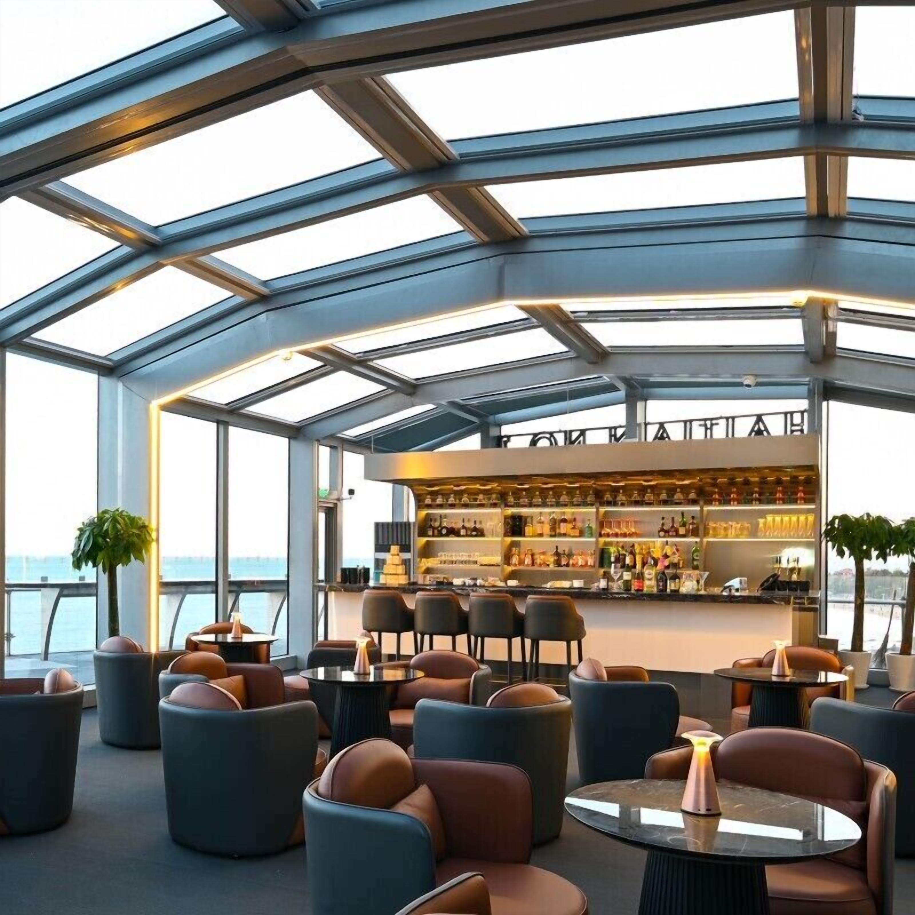 A modern bar area with a glass ceiling, seating with leather chairs, and a bar stocked with bottles.