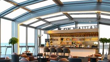 A modern bar area with a glass ceiling, seating with leather chairs, and a bar stocked with bottles.