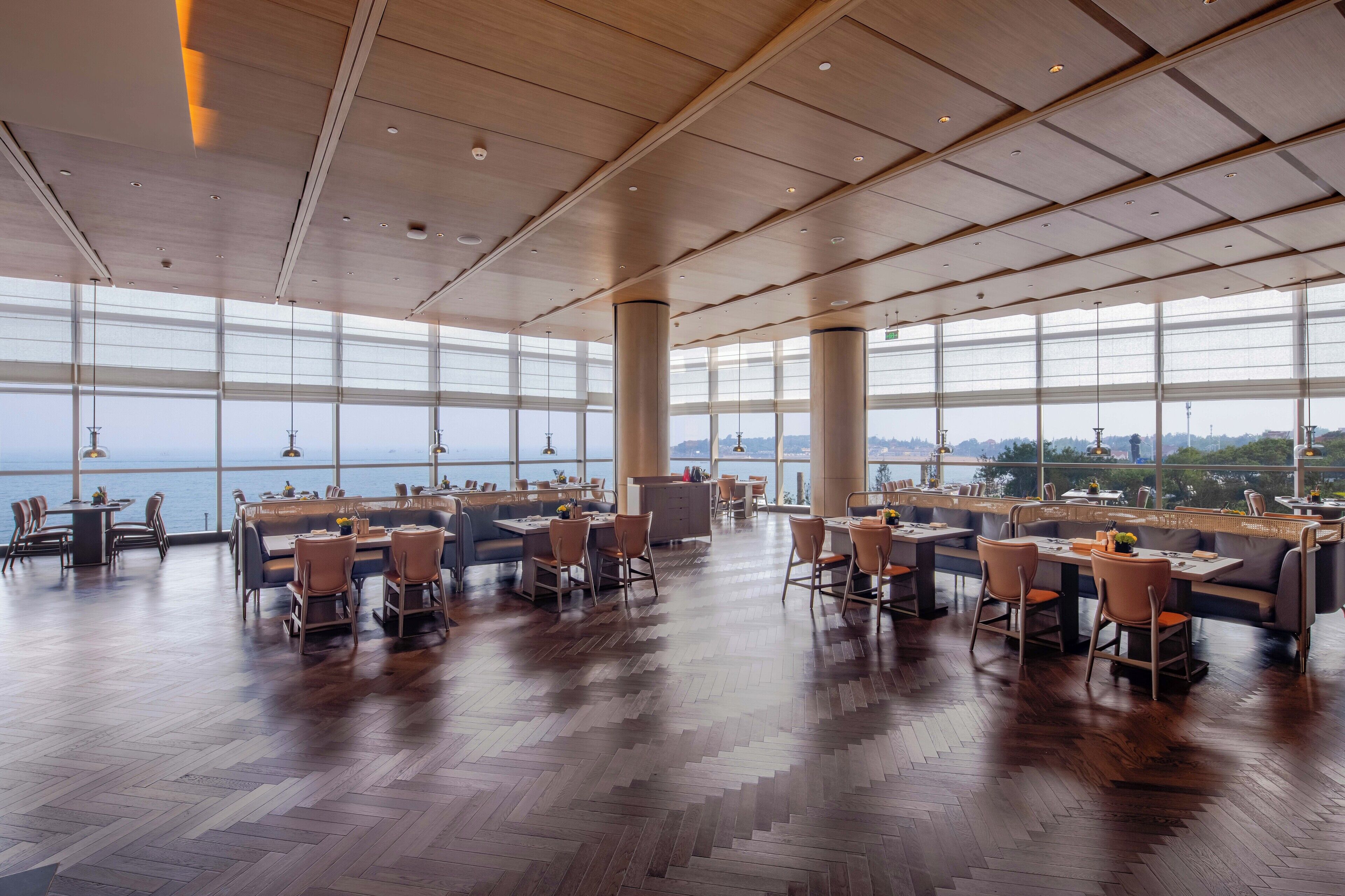 A spacious restaurant with high ceilings, large windows, and a view of the sea.