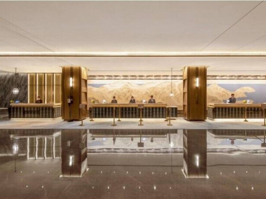 A modern hotel lobby with a reflective floor, a reception desk, and a mural of mountains on the wall.