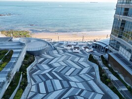 A rooftop terrace with a geometric tile pattern, seating areas, and a view of the beach and ocean.