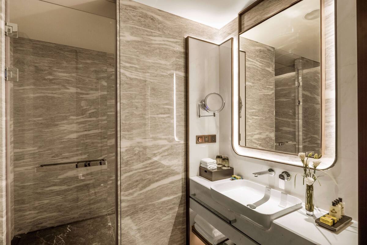 Een moderne badkamer met een glazen douchecabine, een grote spiegel en een witte wastafel met toiletartikelen.