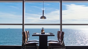 Een tafel met twee stoelen voor een groot raam met uitzicht op de zee.