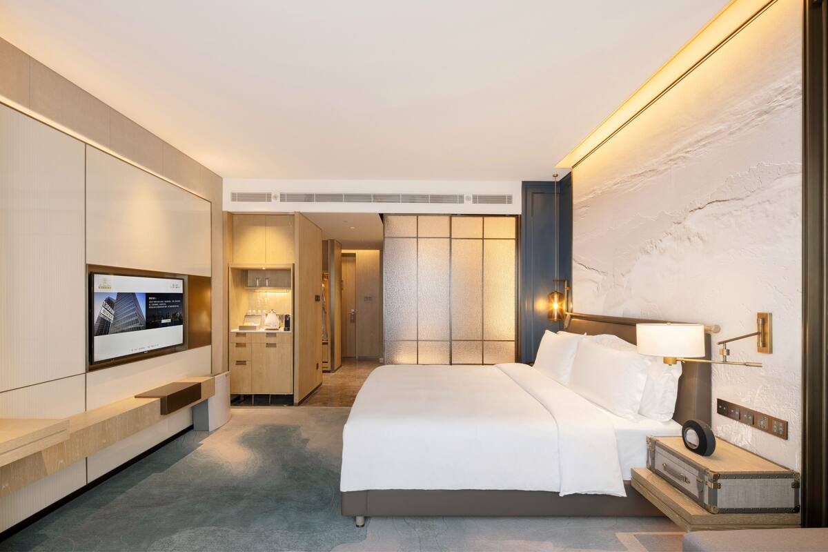 Een moderne hotelkamer met een groot bed, een flatscreen televisie, een nachtkastje en een wandlamp.