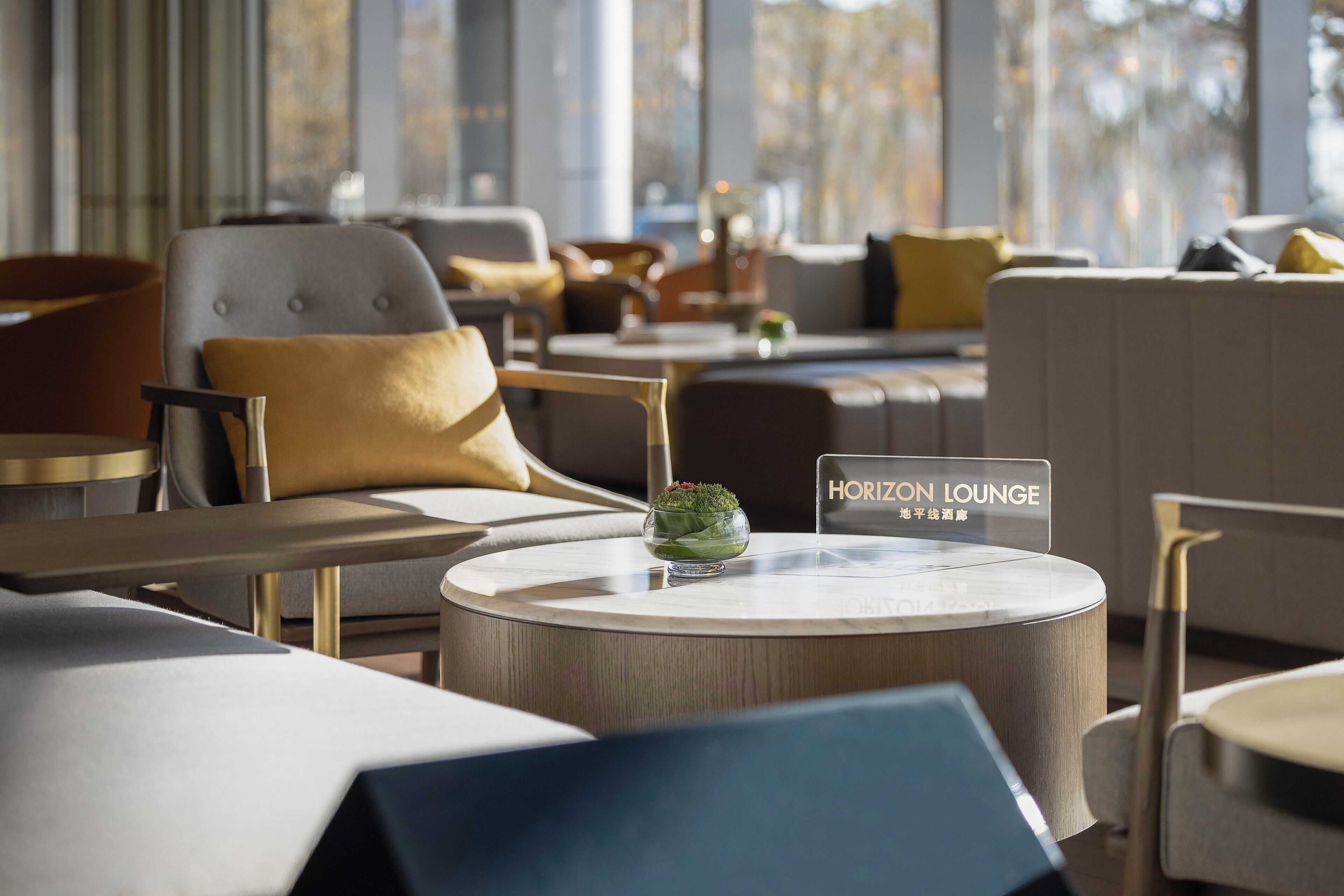Un área de lounge moderna con mesas redondas, asientos cómodos y un cartel con el nombre 'Horizon Lounge'.