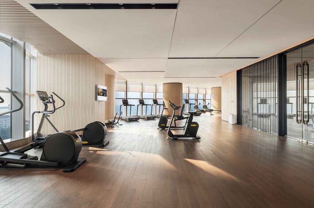 A modern gym with treadmills, ellipticals, and a large window providing a view of the city.