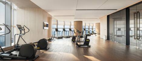 A modern gym with treadmills, ellipticals, and a large window providing a view of the city.