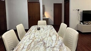 Ein Konferenzraum mit einem Marmortisch, weißen Stühlen, einer Kristallleuchtre und einem Fernseher auf einem Podest.