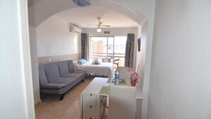 A compact living space with a sofa, a small table, a ceiling fan, and a view of the outside balcony.