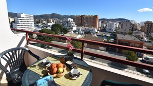 A balcony with a table set for breakfast, overlooking a cityscape with buildings and mountains.