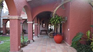 Un pasillo con arcos, piso de baldosas y plantas en macetas.