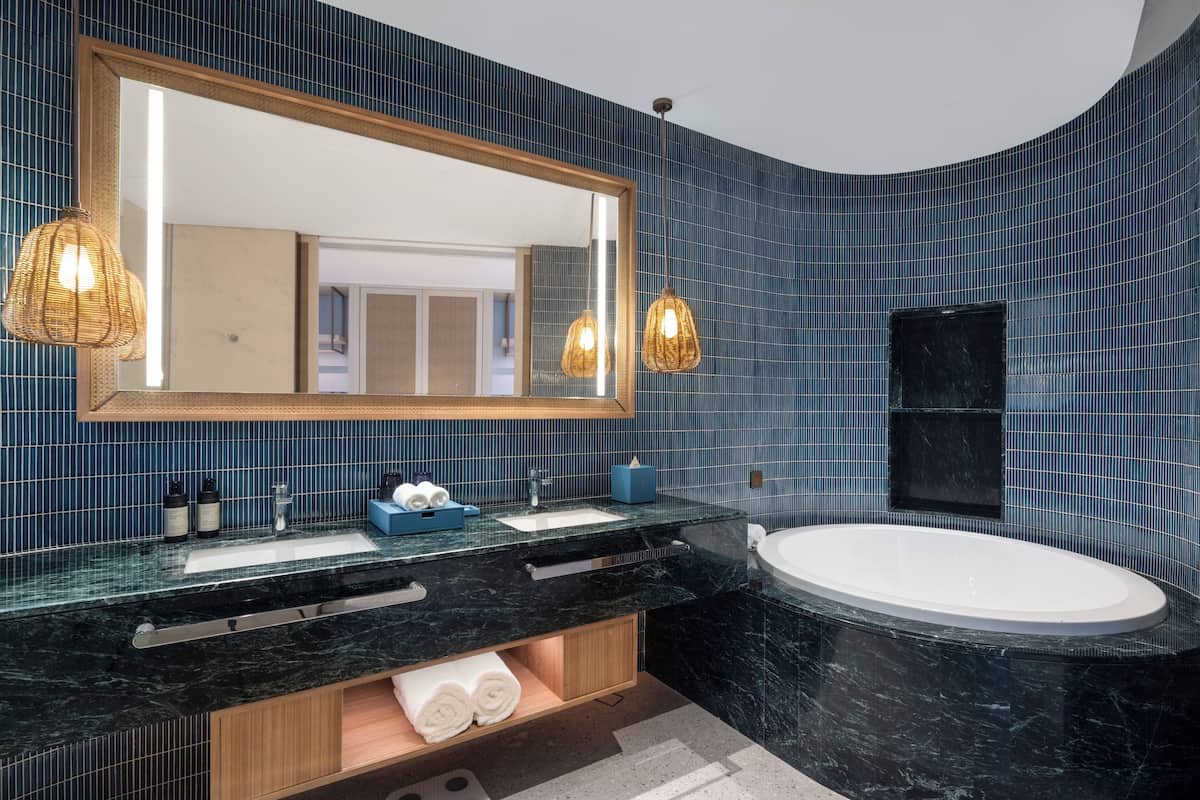 A modern bathroom with a black marble sink, a large mirror, and a freestanding bathtub.