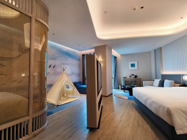Une chambre d’hôtel moderne dotée d’un grand lit, d’un coin salon avec un canapé et des fauteuils, d’un petit bureau avec une chaise et d’une structure ressemblant à une tente.