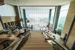 Un intérieur spacieux et moderne, doté d’un escalier central, de coins salon et de grandes fenêtres offrant une vue sur l’extérieur.