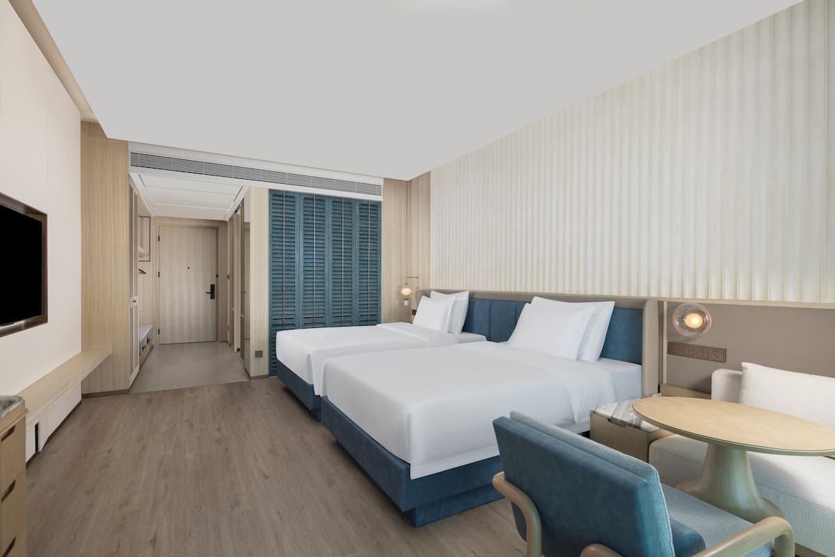 A hotel room with two beds, a TV, a desk, and a chair.