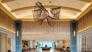 Eine geräumige Lobby mit hoher Decke, modernen Kronleuchtern und einer Rezeption mit großem Empfangstresen und Sitzgelegenheiten.