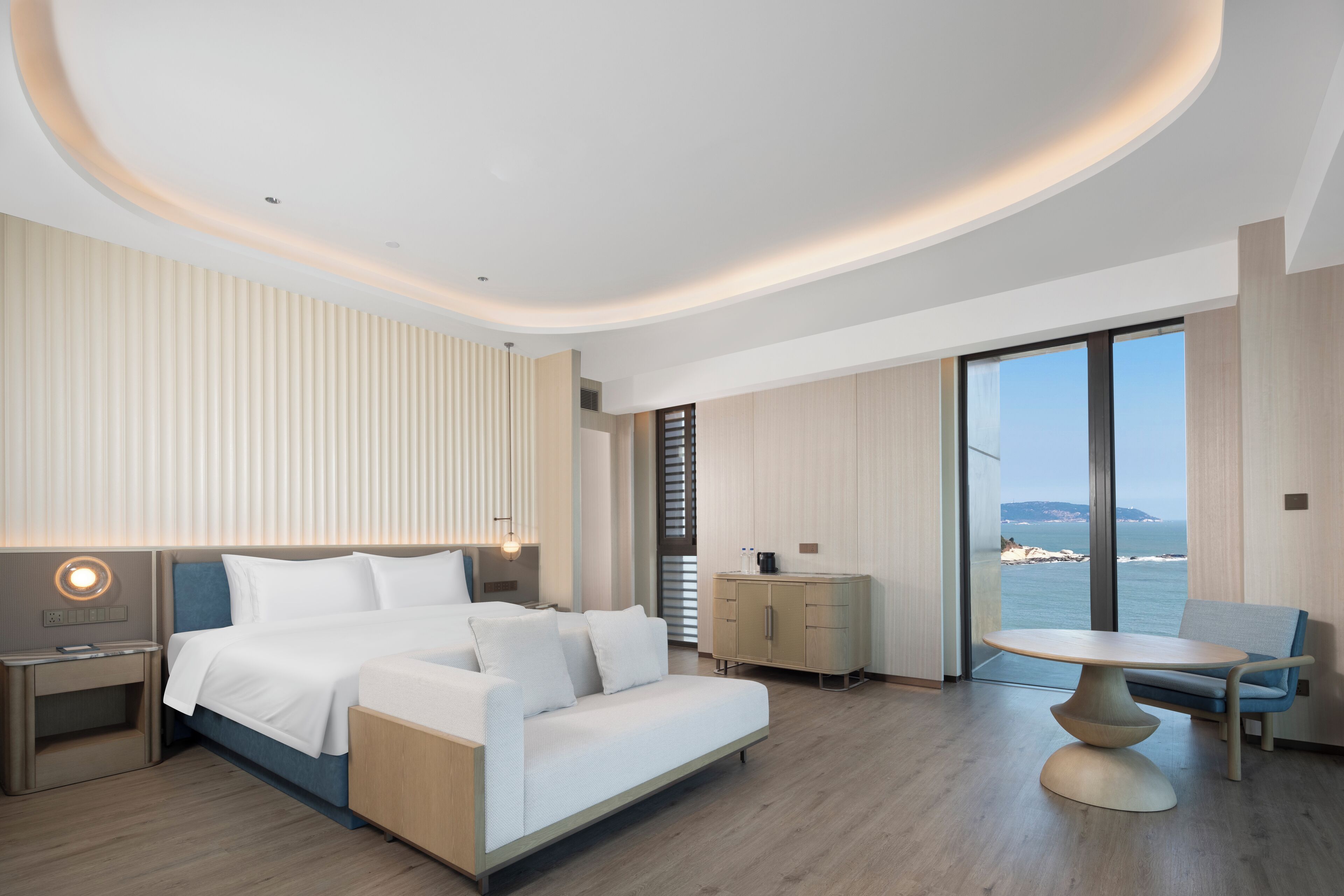 Ein modernes Hotelzimmer mit Bett, Schreibtisch, Stuhl und Meerblick.