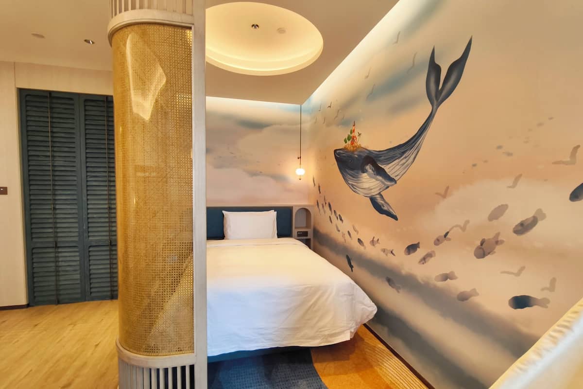 A modern hotel room with a large bed, a decorative wall mural, a unique cylindrical column, and a ceiling light fixture.