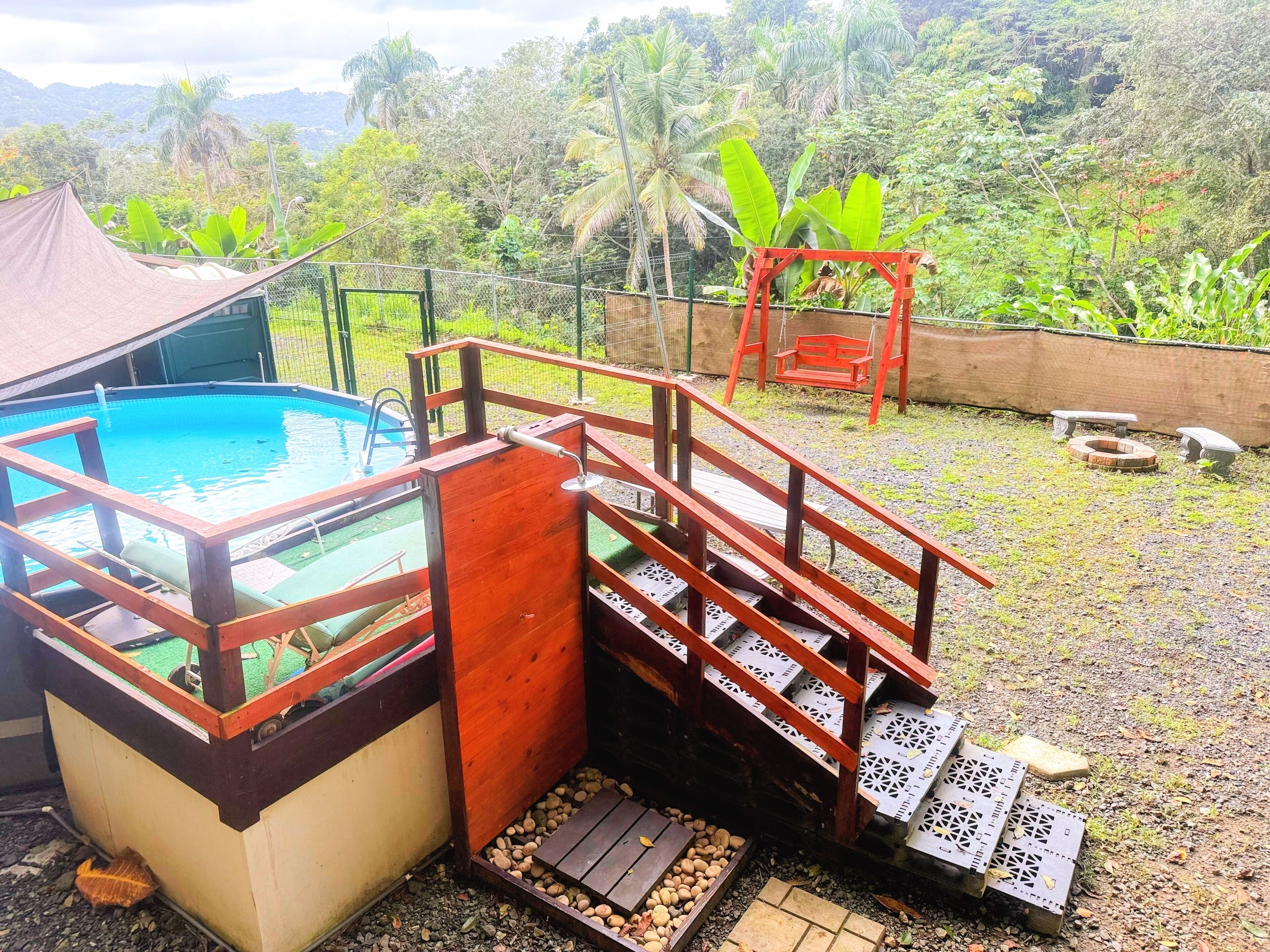 Una piscina con un deck de madera y una pequeña escalera de madera que lleva a un área techada.