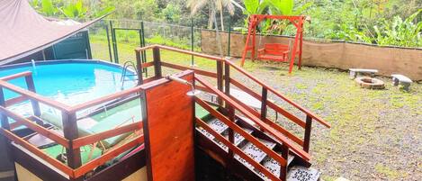 Una piscina con un deck de madera y una pequeña escalera de madera que lleva a un área techada.