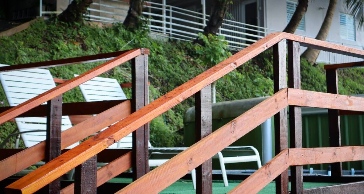 Uma escadaria de madeira leva a uma área de piscina com espreguiçadeiras e um gramado verde.