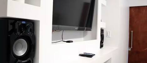 En moderne stue med et fladskærms-tv monteret på et hvidt tv-møbel, en sort højttaler og en fjernbetjening på møblet.