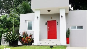 A modern two-story house with a red door, white walls, and a small front porch. - Mystic River Retreat | 3BR/2BA•Pool - Jacuzzi - Beverly Hills, Guaynabo, Guaynabo, Puerto Rico (Guaynabo)